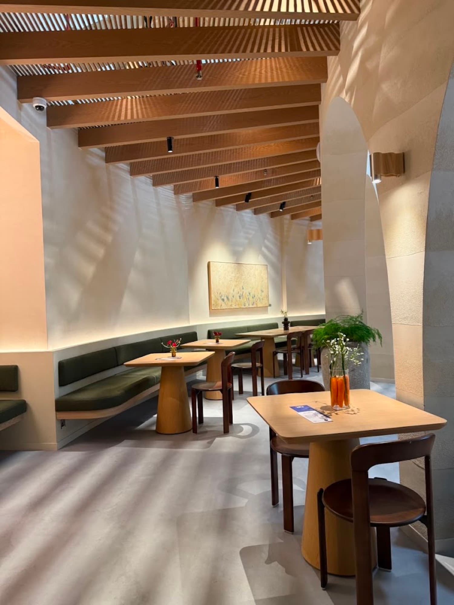 Oak tables and olive banquettes under timber ceiling slats