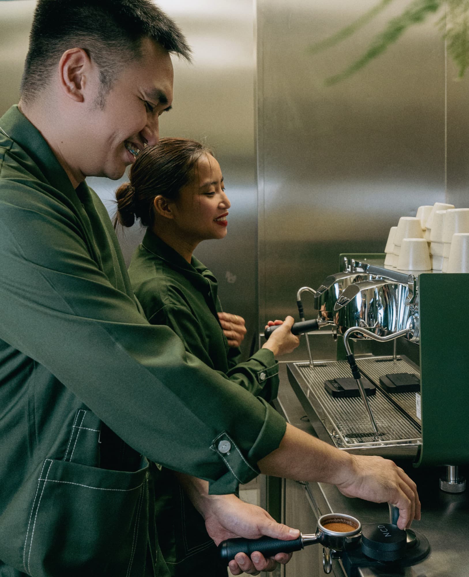 Two baristas in olive-green uniforms pulling espresso at the counter